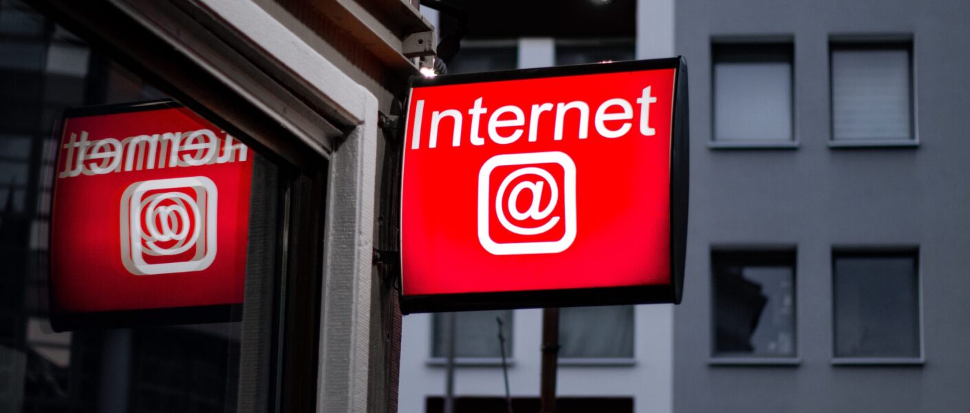 A sign written "Internet @" in a corner with a building behind.